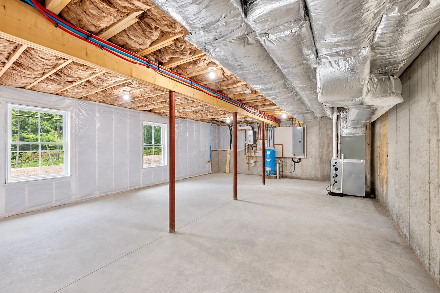 Basement with fiberglass batts between exposed ceiling joists, large silver HVAC ducts overhead, and a clear concrete floor.