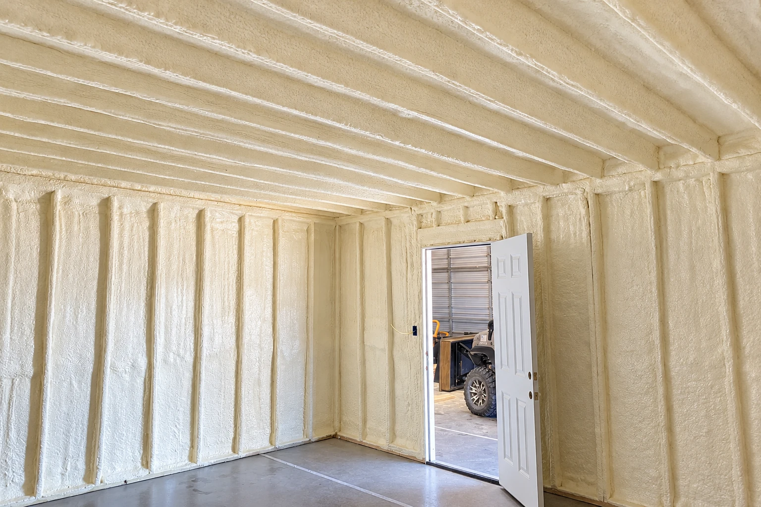 Cream-colored spray foam coats the walls and ceiling of a commercial room beside an open door.