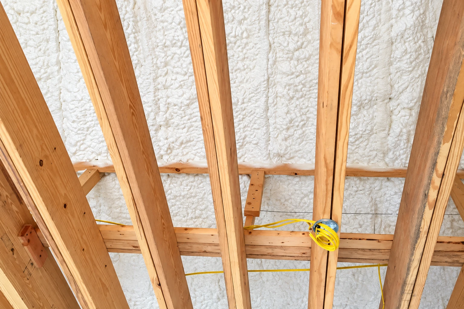 White spray foam fills the spaces behind exposed wooden framing in a house under construction.